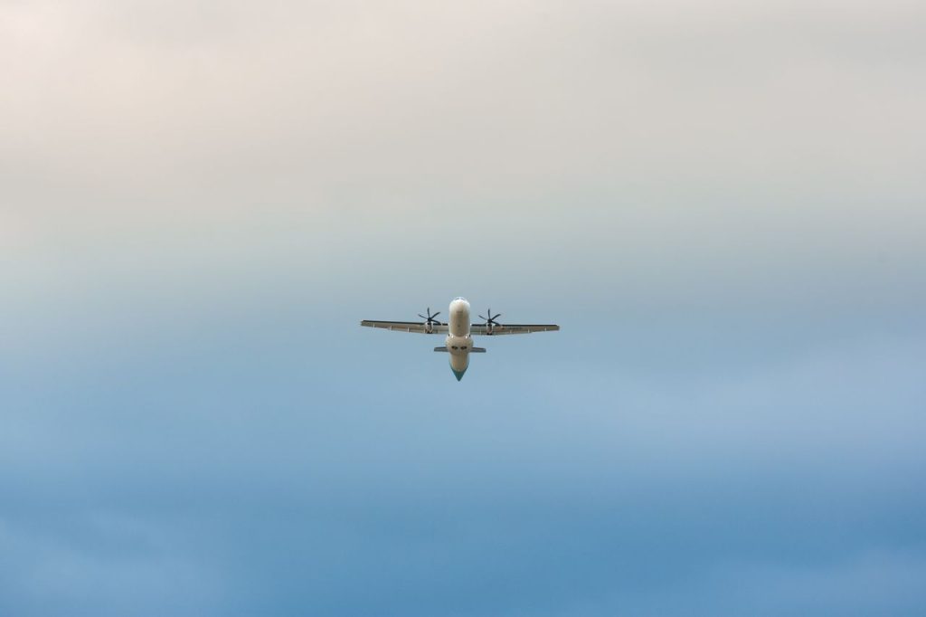 A propeller airplane mid-flight against a clear blue sky, captured from below.