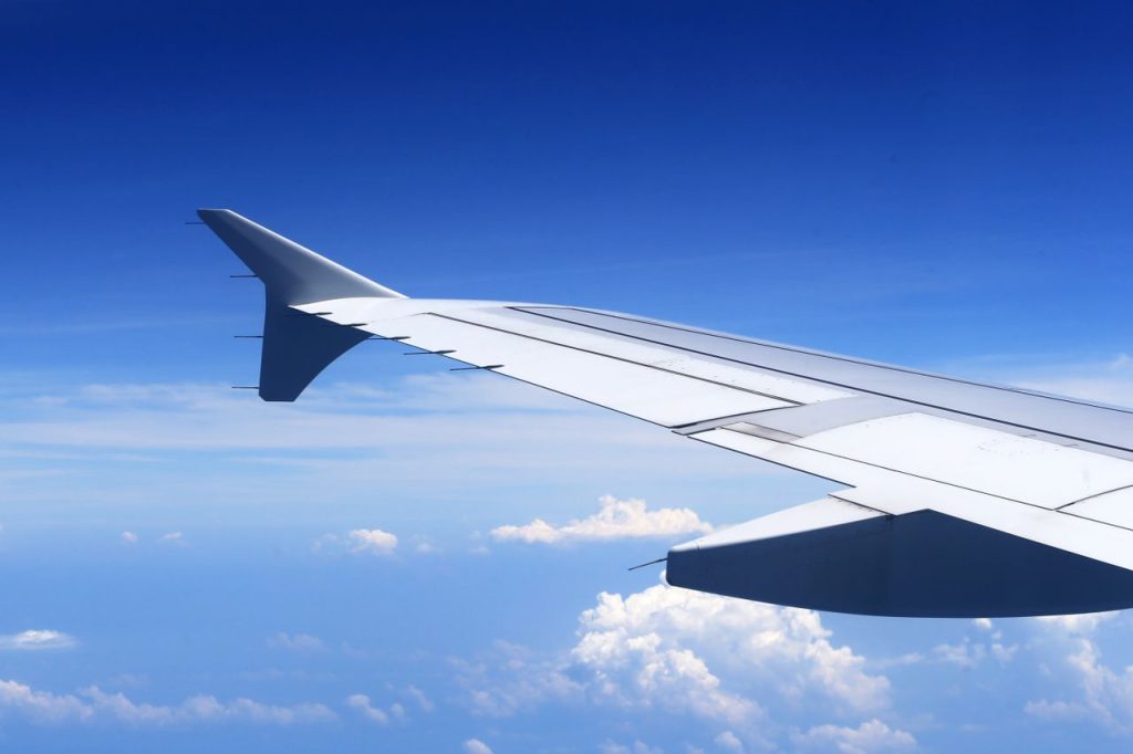 A stunning view from an airplane window showing a wing against a clear blue sky and clouds.